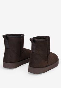 Stivaletti in suede marrone con fodera morbida, punta arrotondata e suola in gomma texturizzata. Presentano linguette abbinati sul retro.