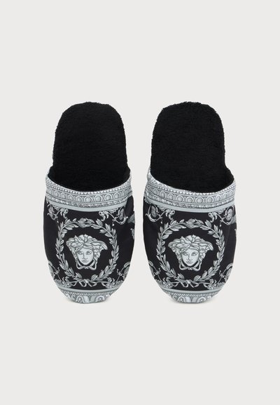 Ζευγάρι μαύρα παντόφλες τύπου slip-on με λευκά περίτεχνα σχέδια και μοτίβα με κεφάλι Μέδουσας στην κορυφή.