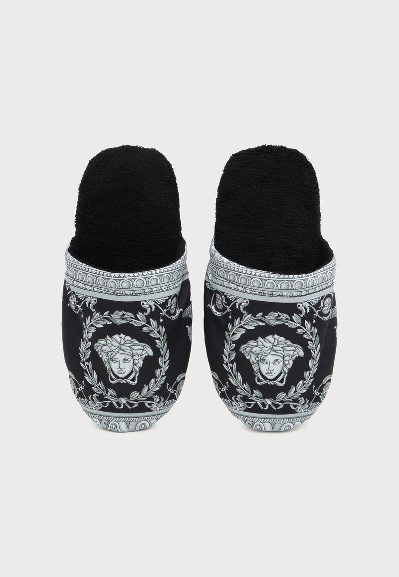 Pair of black slip-on slippers with white intricate patterns and Medusa head motifs on top.