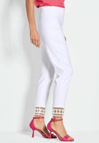 Witte broek met gedetailleerde borduursels aan de zoom, gecombineerd met roze stilettohakken. De stof lijkt lichtgewicht en glad.