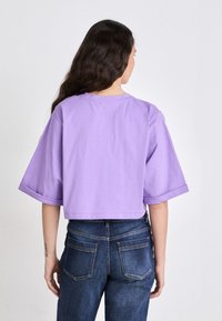 Cropped, short-sleeve t-shirt in light purple cotton with rolled sleeves, paired with dark blue denim jeans featuring back pockets.