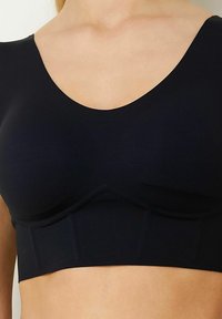 Reggiseno sportivo nero realizzato in tessuto liscio, con scollatura a barca, spalline larghe e un elastico nella parte inferiore per il sostegno.