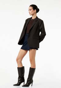 Brunternetternet oversized blazer, mørkebrun top, marineblå shorts og knæhøje sorte læderstøvler med spidse tæer og stilettohæle.