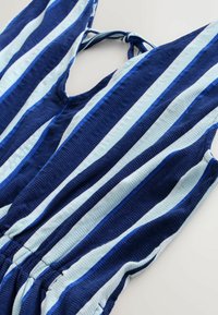 Sinivihreät ja vaalean siniset raidalliset hihattomat haalari, jossa on v-pääntie, joustava vyötärö ja teksturoitu kangas. Sidotaan olkapäiltä.