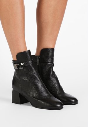 Zwarte leren enkellaarsjes met een gestructureerde afwerking, vierkante hak, puntige neus en zilveren gesp detail bij de boorden. Ritssluiting aan de zijkant.