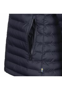 Marineblå boblejakke med kviltet design, som har en glidelåslomme og liten svensk flaggdetalj ved kanten. Glatt, syntetisk tekstur.
