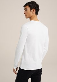 Camiseta blanca de manga larga hecha de una tela suave, con cuello redondo y un diseño ajustado, combinada con jeans oscuros para crear contraste.