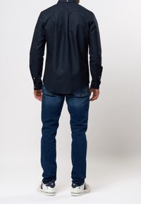 Granatowa koszula z długim rękawem, mankiety na guziki, gładki bawełniany materiał, dopasowany krój, zestawiona z niebieskimi dżinsami i białymi trampkami.