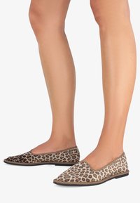 Scarpe flat con stampa leopardata, upper in tessuto liscio, punta arrotondata e suola flessibile. Toni neutri e rifiniture sottili arricchiscono il design.