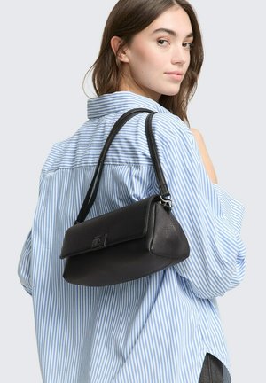 Borsa a tracolla in pelle nera con superficie texturizzata, forma strutturata e chiusura a patta, indossata sulla spalla con una tracolla sottile.