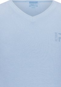 Jasnoniebieska koszulka V-neck z miękkiego materiału, z małym szarym logo "RETOUR" na przedniej stronie. Gładka tekstura, casualowy design.