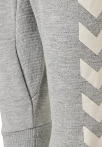Grå sweatpants med en mjuk textur, med ett vitt zickzackmönster längs sidan. Inkluderar en sidoficka och ribbade anklar.