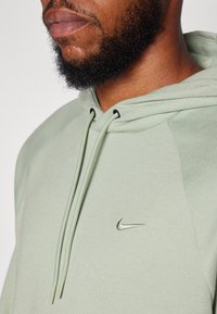 Lysegrønn Nike hettegensser med snorer, har en sølvlogo på brystet, laget av myk stoff med teksturerte ermer.