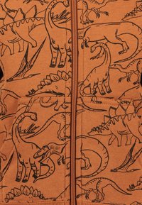 Felpa arancione con illustrazioni di dinosauri neri, dotata di zip frontale, tasche e un tessuto morbido e testurizzato.