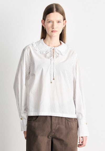 Blouse à rayures blanches avec un col à volants, un col noué, et des manches longues. Présente des accents dorés aux poignets et une coupe décontractée.