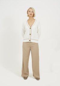 Biała swetrowa kardigan z głębokim dekoltem w serek, w beżowe akcenty oraz z dużymi guzikami, zestawiony z beżowymi, szerokimi spodniami oraz taupe'owymi balerinami.