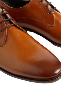 Chaussures de ville en cuir marron avec un bout pointu, finition lisse et lacets noirs. Présentent des coutures discrètes sur les côtés.