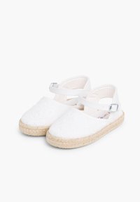 Sandales espadrilles blanches avec une tige en tissu texturé, un bout rond et une semelle en corde de jute. Comprend une bride à la cheville avec une boucle en métal.