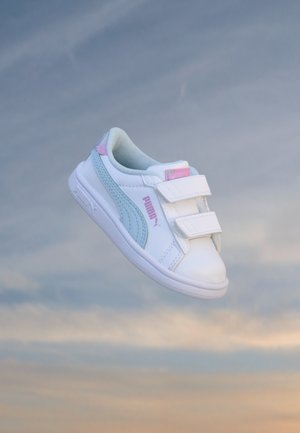 Chaussure pour tout-petit Puma blanche et bleu clair avec des accents roses et deux brides velcro flottant sur un fond de ciel doux et nuageux.