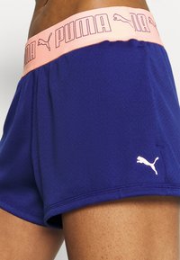 Paarse sportshorts met een roze PUMA-logo op de tailleband en een klein wit logo aan de zijkant, met een gladde, lichte textuur.