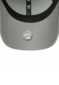 Gorra gris con visera negra, que presenta un logo circular de la MLB que se asemeja a una pelota de béisbol en la parte delantera. Tejido texturizado con detalles de costura visibles.