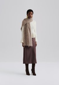 Pull en tricot blanc, jupe en satin marron, et écharpe en peluche marron. Des bottes marron jusqu'aux genoux complètent la tenue. Design simple et épuré.