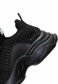 Black athletic shoe with a mesh upper, textured accents, and a thick rubber sole featuring contouring details and circular cutouts.