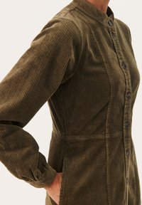 Robe en velours côtelé vert olive avec un col mandarin, boutonnage sur le devant et texture côtelée verticale ; comprend des manches bouffantes et des poches latérales.