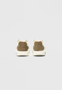 Smeđi nubuk i bijela tkanina tenisica s podstavljenim potplatom, s niskim profilom i utisnutim logom na stražnjem dijelu.