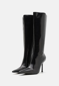 Støvler i sort læder, der går til knæene, med en blank finish, spidse tæer og høje stilettohæle. Har et sømløst design og lynlås på siden.