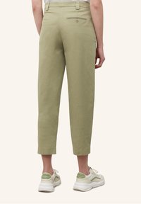 Lichtgroene, gekorte broek van katoen met een achterzak en een knoopdetail. gedragen met witte en groene sneakers.