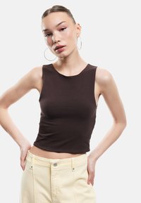 Top sans manches marron en tissu lisse, avec un col rond et une coupe ajustée, associé à un jean de couleur claire.