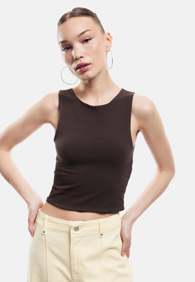 Top sans manches marron en tissu lisse, avec un col rond et une coupe ajustée, associé à un jean de couleur claire.