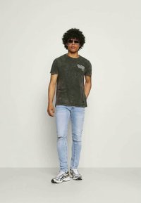 T-shirt texturado cinza escuro com decote redondo e logotipo estampado, combinado com jeans skinny desgastados azul claro e tênis esportivos.