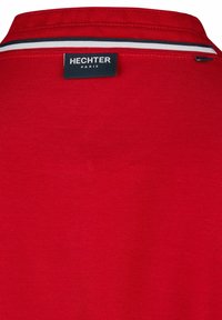 Rode polo met een gestructureerde stof, met een klassieke kraag. Het label vermeldt "HECHTER PARIS," versierd met witte en marineblauwe strepen.