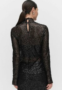 Haut à manches longues en sequins noirs avec un col montant et un détail en trou de serrure à l'arrière, présentant une finition texturée et scintillante. Silhouette lisse et ajustée.