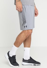 Ljust grå träningsshorts med svarta detaljer och en meshsidedel, i kombination med svarta sneakers, vita strumpor och en grå t-shirt.