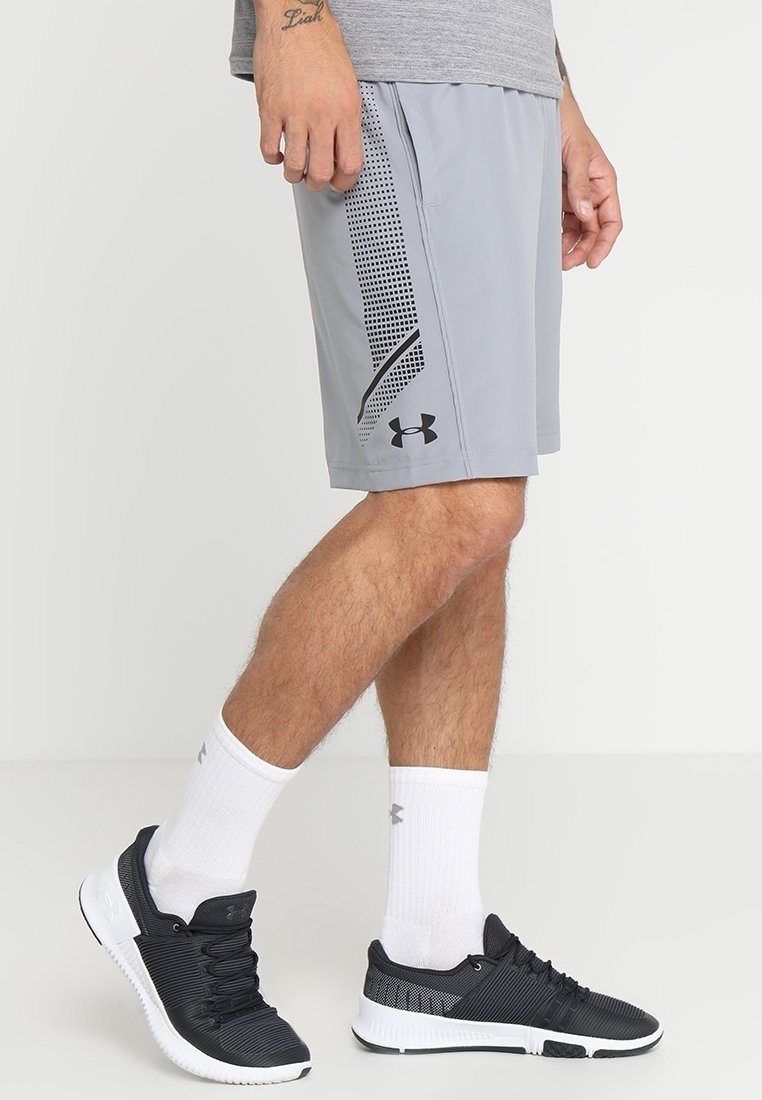 Lichtgrijze sportshorts met zwarte accenten en een mesh zijpaneel, gecombineerd met zwarte sneakers, witte sokken en een grijs T-shirt.