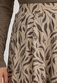 Falda beige con patrones oscuros de hojas y flores, con una cintura ajustada y pliegues, hecha de tela suave. Parte superior de manga larga visible arriba.
