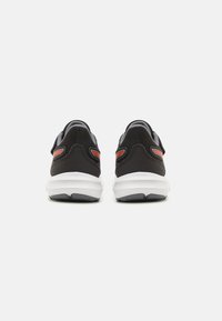 Black athletic shoes with mesh fabric, a white midsole, and red accents on the heel. Textured surface and padded collar detail.