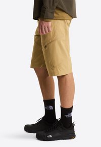 Spodenki khaki z kieszeniami na zamek, wykonane z lekkiego materiału o luźnym kroju, w zestawieniu z czarnymi butami trekkingowymi i skarpetkami z logo.