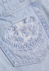 Ετικέτα από ανοιχτό μπλε τζιν με λευκό κεντημένο λογότυπο και σχέδιο κορώνας με το κείμενο «JUICY COUTURE», υφασμάτινη υφή και διαμάντι σχήματος.