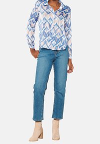 Camicia leggera a maniche lunghe con un motivo geometrico blu, rosa e bianco. Abbinata a jeans a gamba dritta di lavaggio medio e stivali alla caviglia beige.