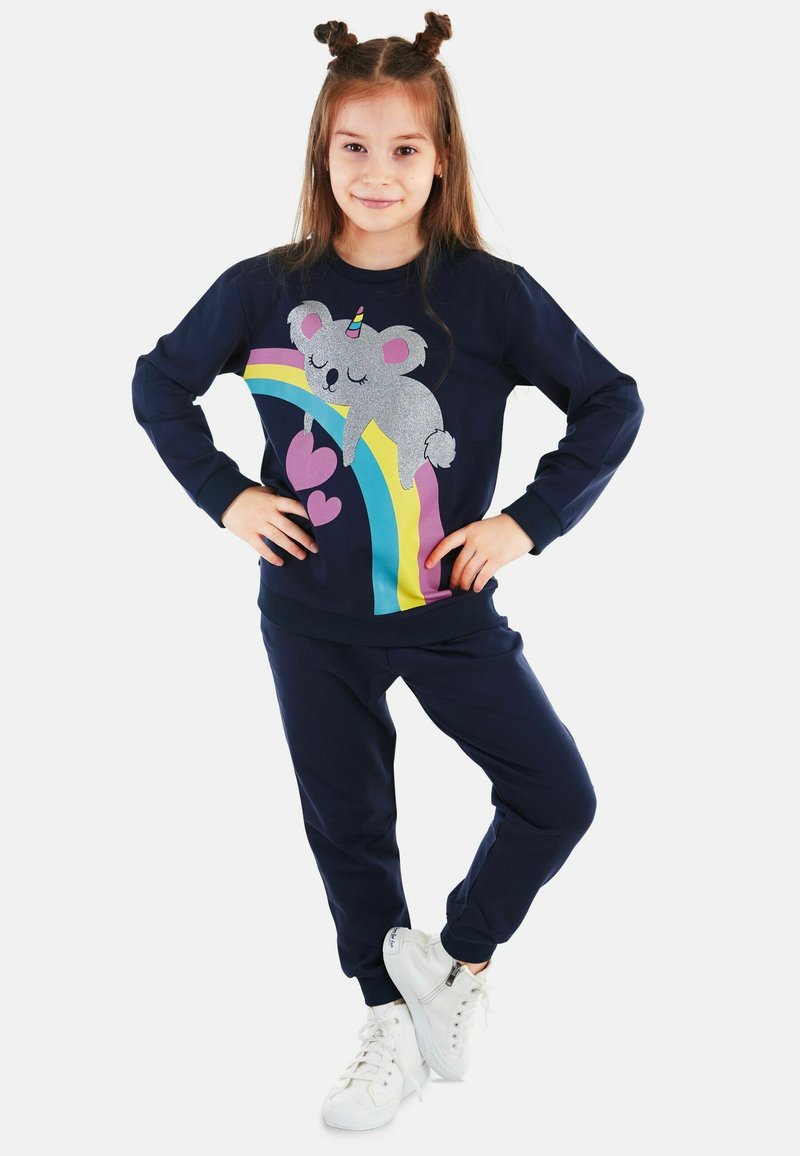 Mornarsko modra longsleeve majica s kapuco z grafiko koale in mavrice; v kombinaciji z usklajenimi hlačami in belimi tenisicami. Mehka tkanina, sproščen kroj.