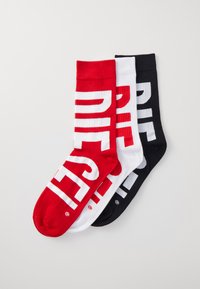 Three pairs of crew socks in red, white, and black. Each has large, contrasting text reading "DIESEL." Ribbed texture and solid colors.