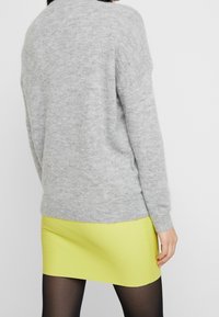 Grau gestrickter Pullover mit langen Ärmeln und rundem Halsausschnitt, kombiniert mit einem leuchtend gelben Minirock. Weiche Textur und lockere Passform.