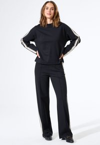 Zwarte sweatshirt en broek met crèmekleurige zijkanten. De top heeft een ronde hals; de broek heeft een getailleerde pasvorm. Glad stofgevoel.