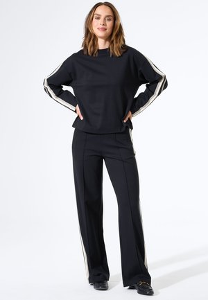 Sweatshirt noir et pantalon avec des rayures crème sur les côtés. Le haut présente un col rond ; le pantalon a une coupe ajustée. Texture de tissu lisse.