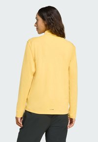 Langärmelig geel shirt van zachte stof. Heeft een hoge kraag en een gestikte zoom, met een klein "climacool" label nabij de onderkant.