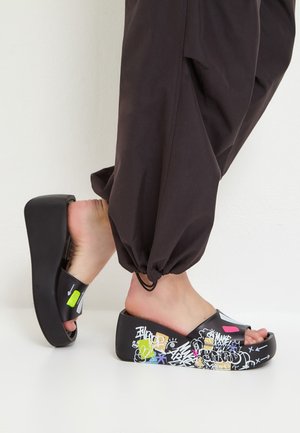 Des sandales à plateforme noires avec des motifs multicolores de style graffiti. Fabriquées en caoutchouc, elles présentent une ouverture à l'avant, un style slip-on et une semelle épaisse.